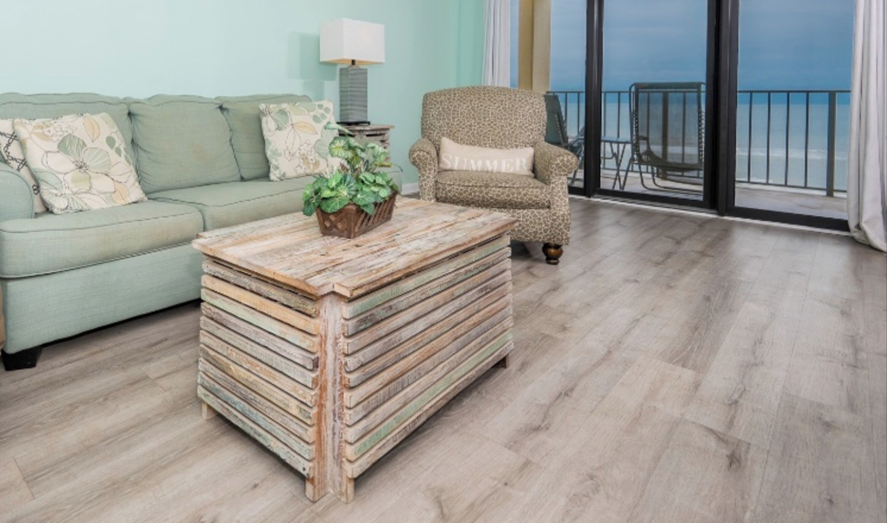 A living room with a sofa, a patterned armchair, a wooden coffee table, and a view of the ocean through large windows.