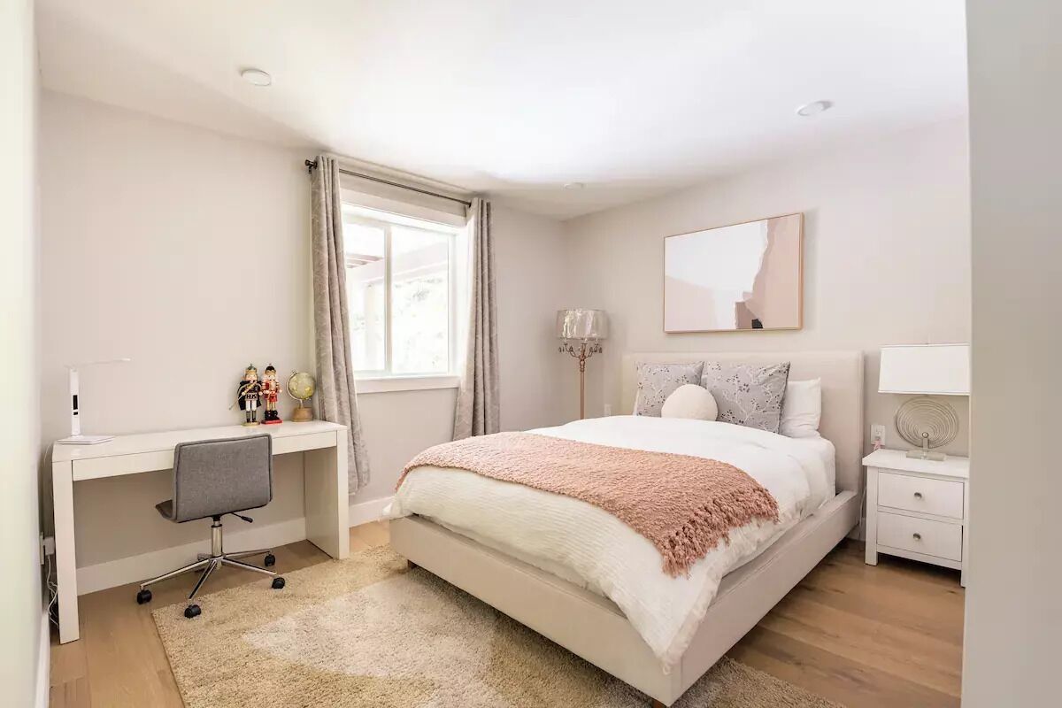 Un dormitorio con cama, escritorio, silla, mesita de noche y ventana con cortinas.