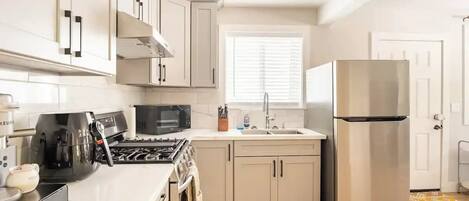 A modern kitchen with white cabinets, a stainless steel refrigerator, a microwave, and a stove.