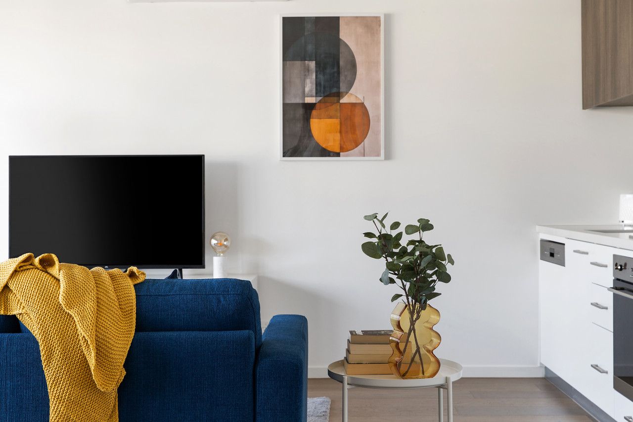 A living room with a blue sofa, a television, a plant, and a painting on the wall.