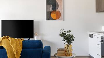 A living room with a blue sofa, a television, a plant, and a painting on the wall.