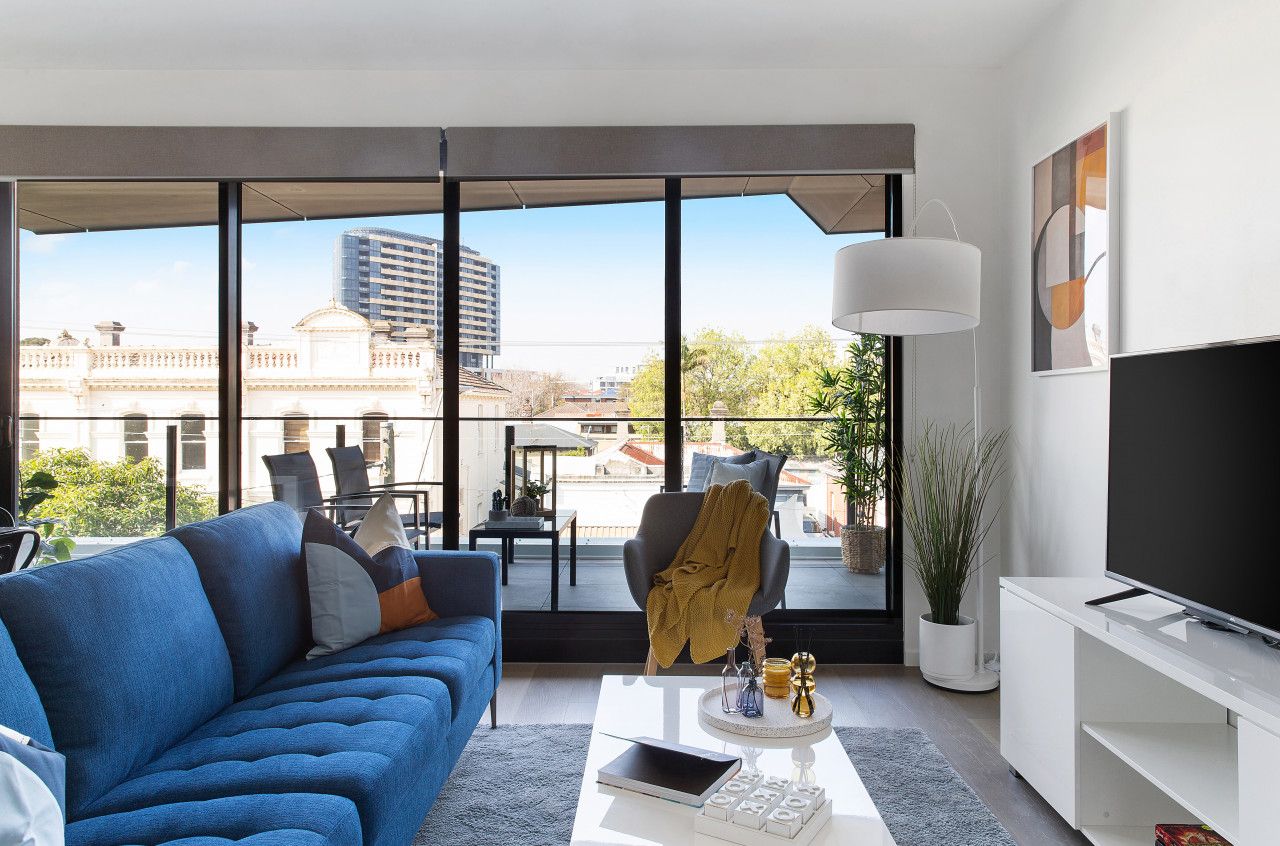 Un salon moderne avec une grande fenêtre, un canapé bleu, une table basse et un téléviseur à écran plat.