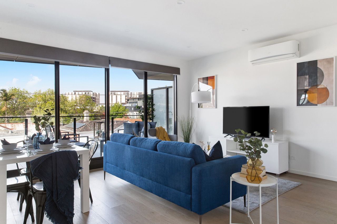 A modern living room with a large blue sofa, a dining table set, and a flat-screen TV.
