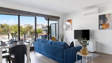 A modern living room with a large blue sofa, a dining table set, and a flat-screen TV.