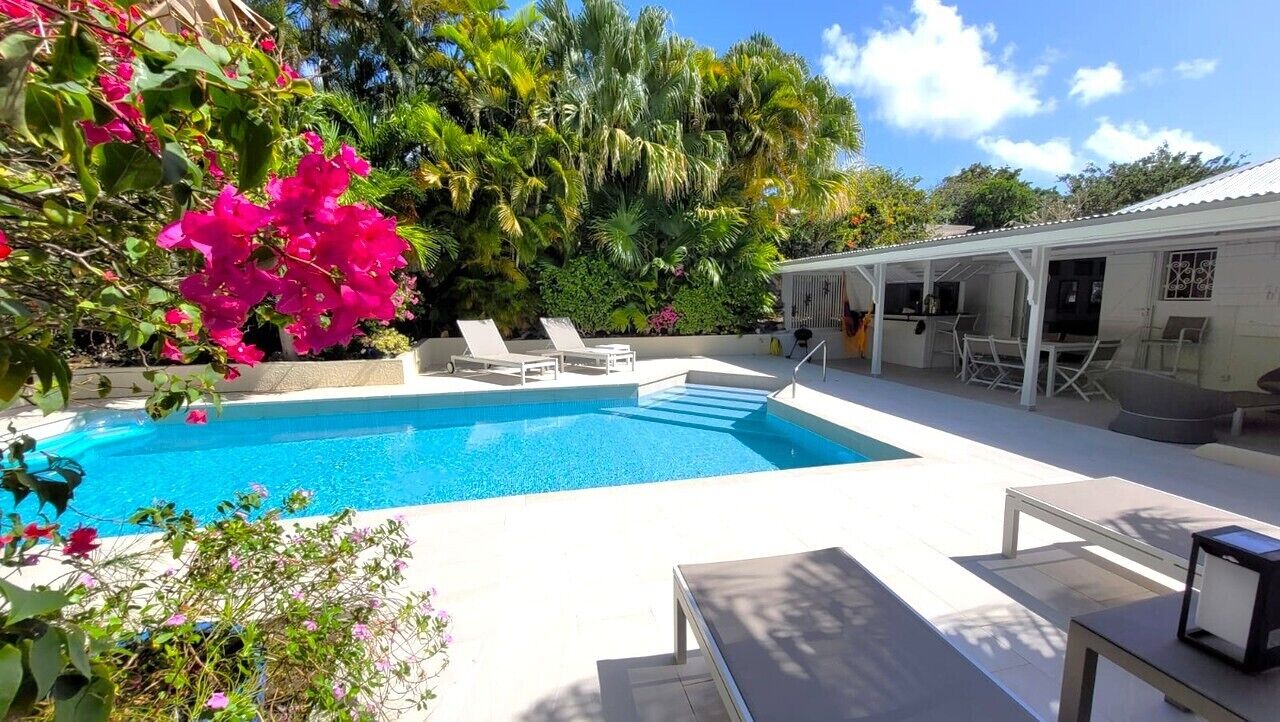 Une piscine avec des chaises longues, un patio couvert et une végétation luxuriante.