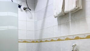 Pieni kylpyhuone, jossa on valkoiset laatat, wc, suihku ja pyyheteline.