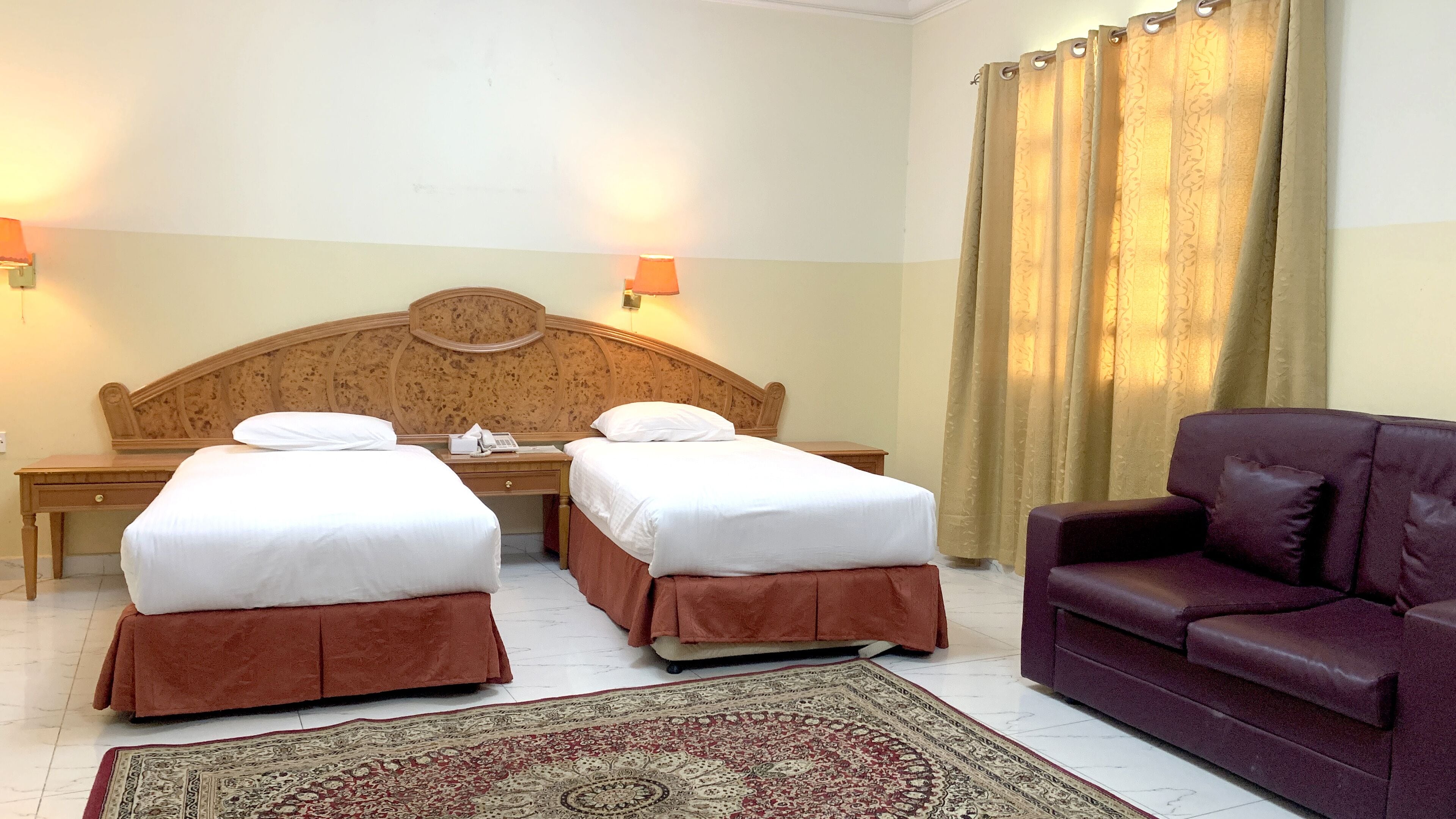 A hotel room with two beds, a desk, a chair, and a large rug.