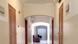 A hotel hallway with marble flooring, wooden doors, and a view of a room with a purple chair. - Super OYO 151 Manam 2 Hotel Apartment (Muscat)