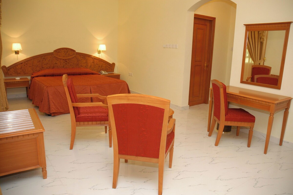 A hotel room with a bed, two chairs, a desk, and a mirror.