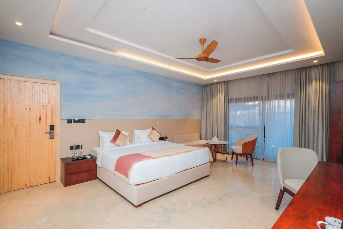 A modern hotel room with a large bed, a desk, a chair, and a ceiling fan.