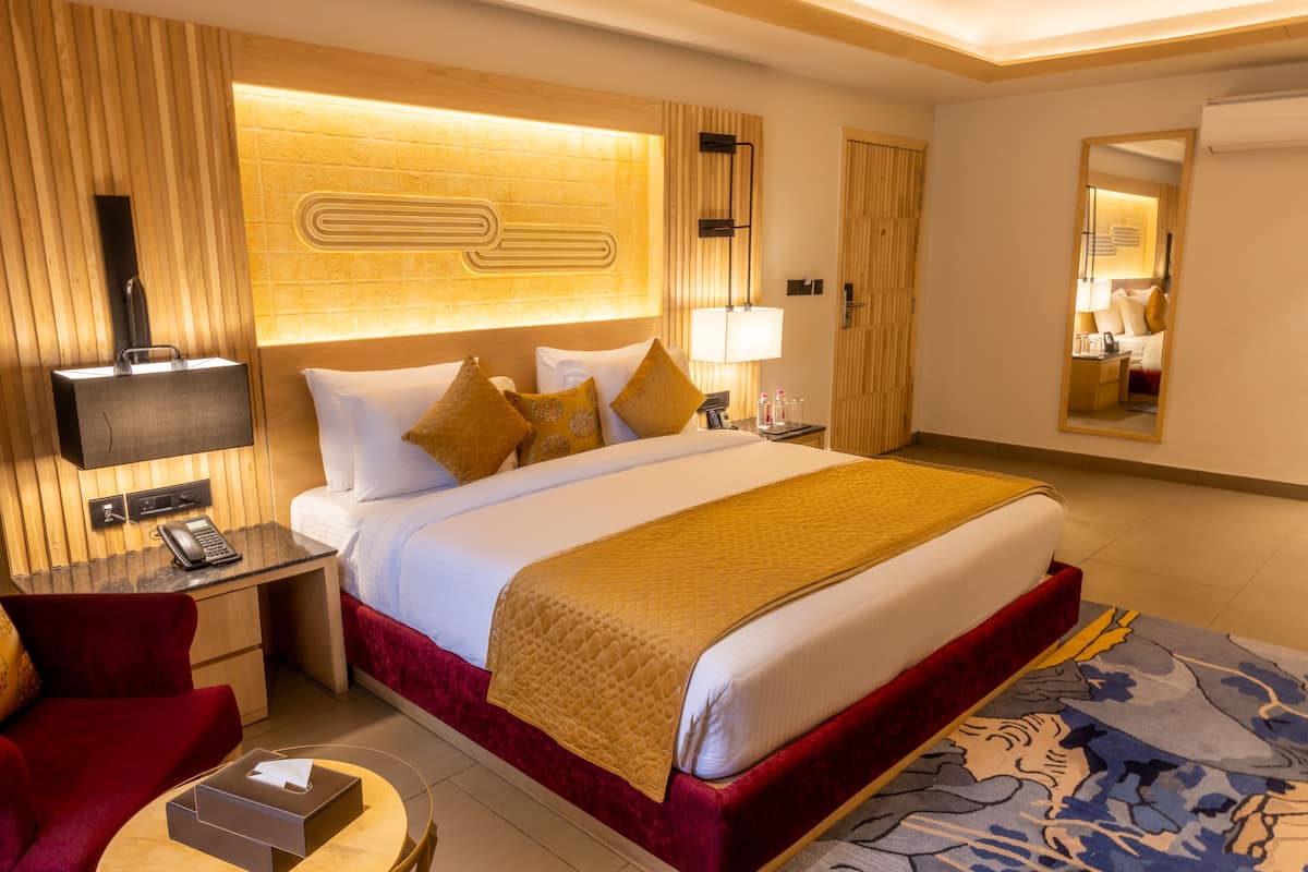 A hotel room with a large bed, a desk with a telephone, a mirror, and a red armchair.