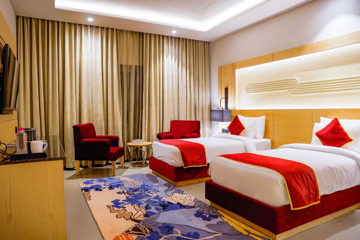 A hotel room with two beds, a desk, a chair, a TV, and a large window with curtains.