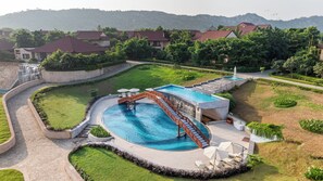 Piscina con tobogán, rodeada de un área ajardinada con césped y árboles.