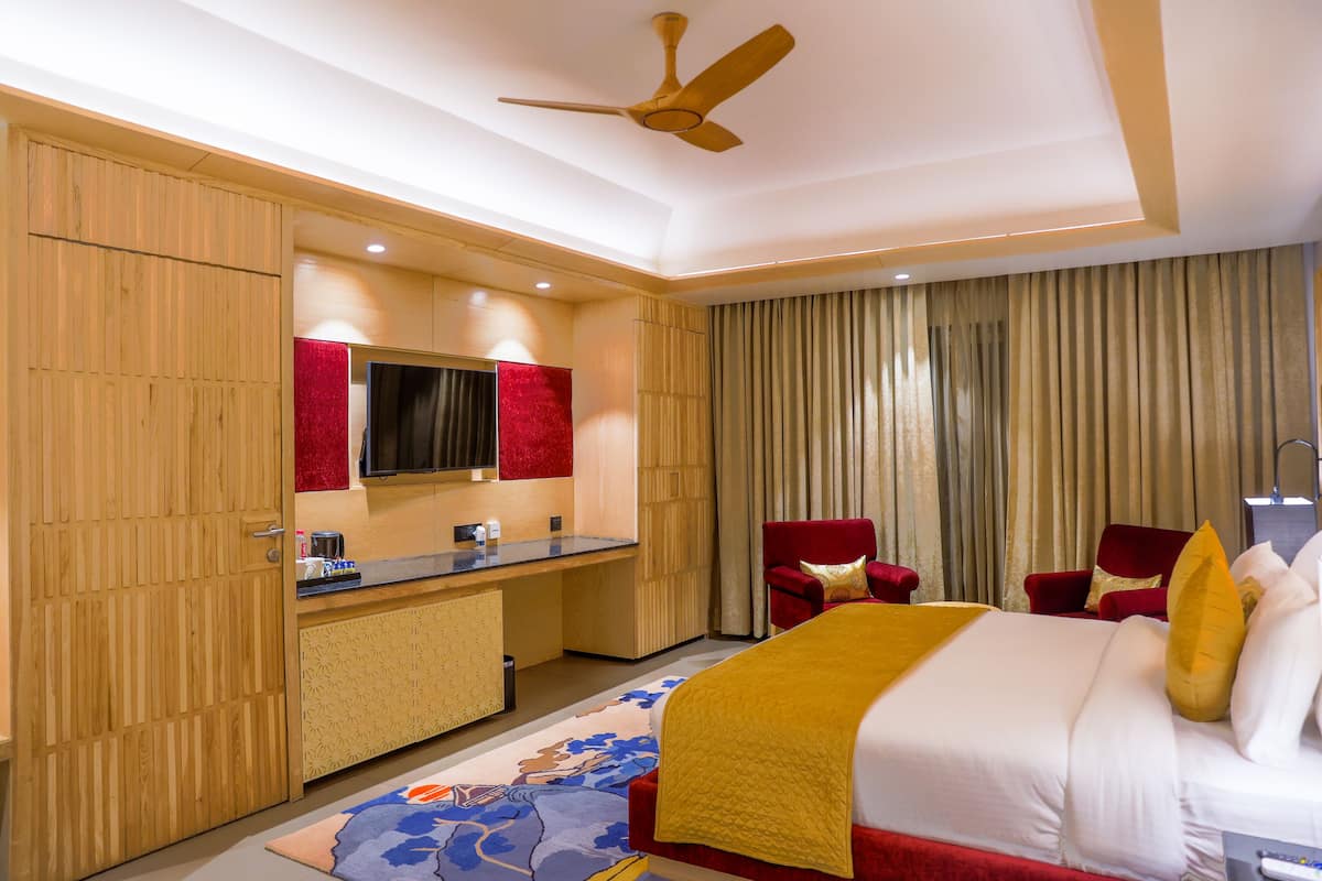A hotel room with a bed, a desk with a mirror, a red chair, and a ceiling fan.