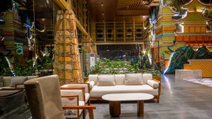 Un lobby espacioso con diseño moderno, que presenta una zona de estar central con sofás y sillones, un pilar decorativo grande y vistas a un edificio de estilo tradicional al fondo.
