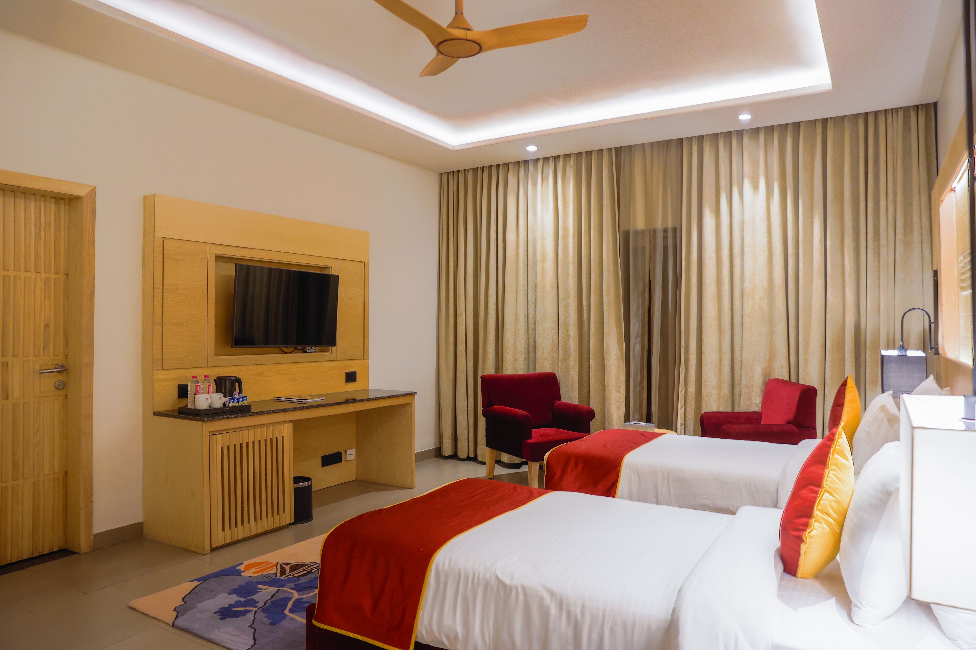 A hotel room with two beds, a desk, a TV, and a red chair.