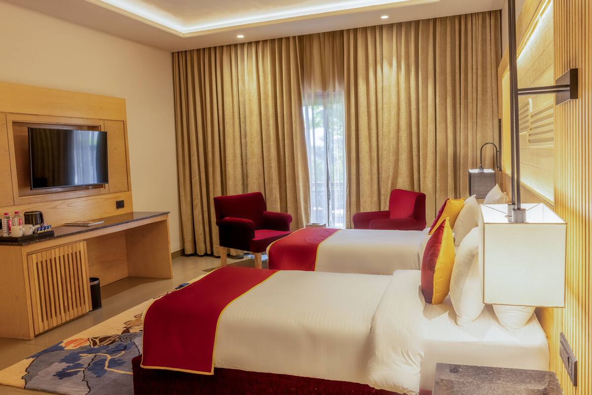 A hotel room with two beds, a desk, a TV, and a window with curtains.
