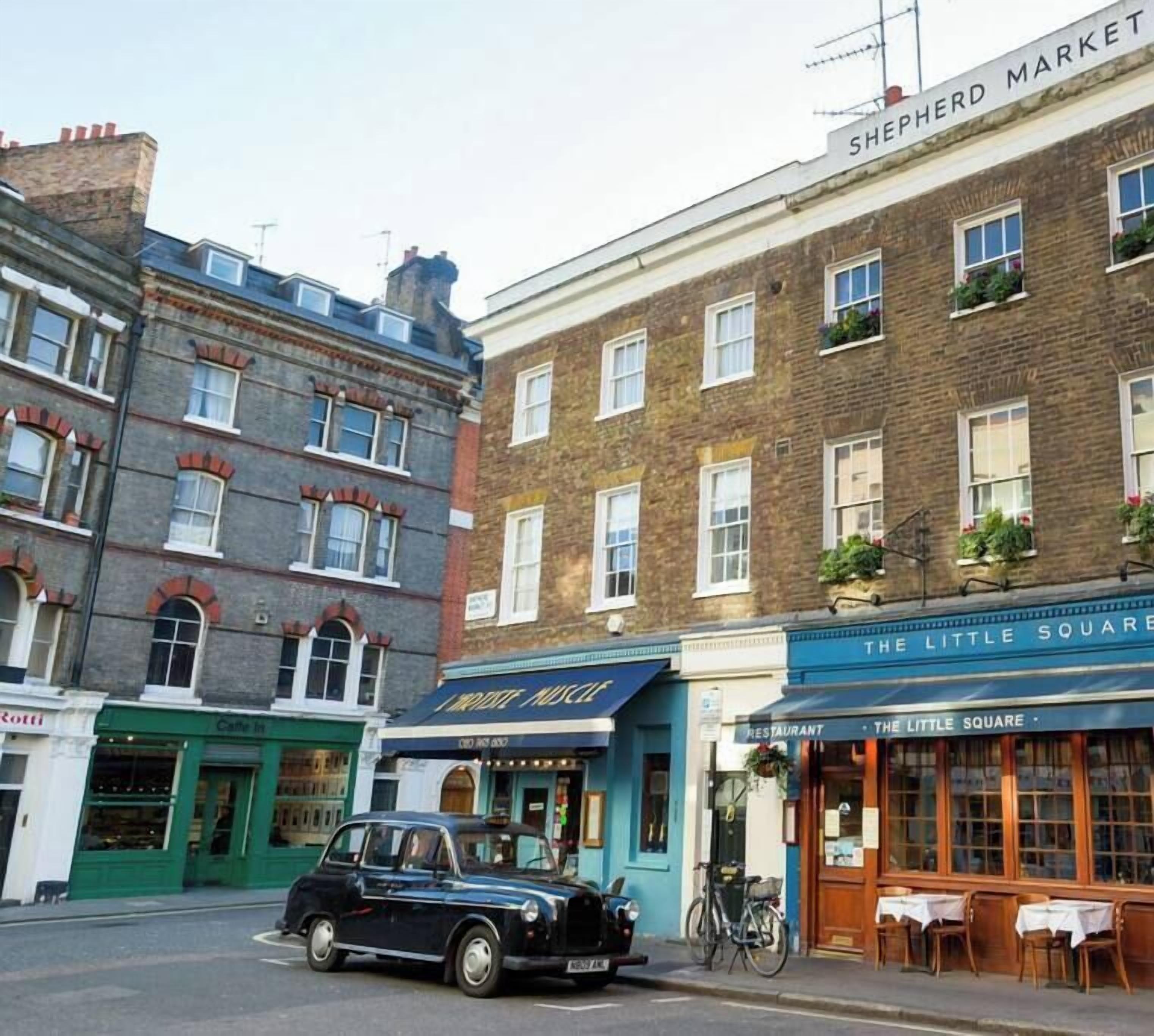 A vintage black car parked on a street with buildings, including a cafe and a restaurant.