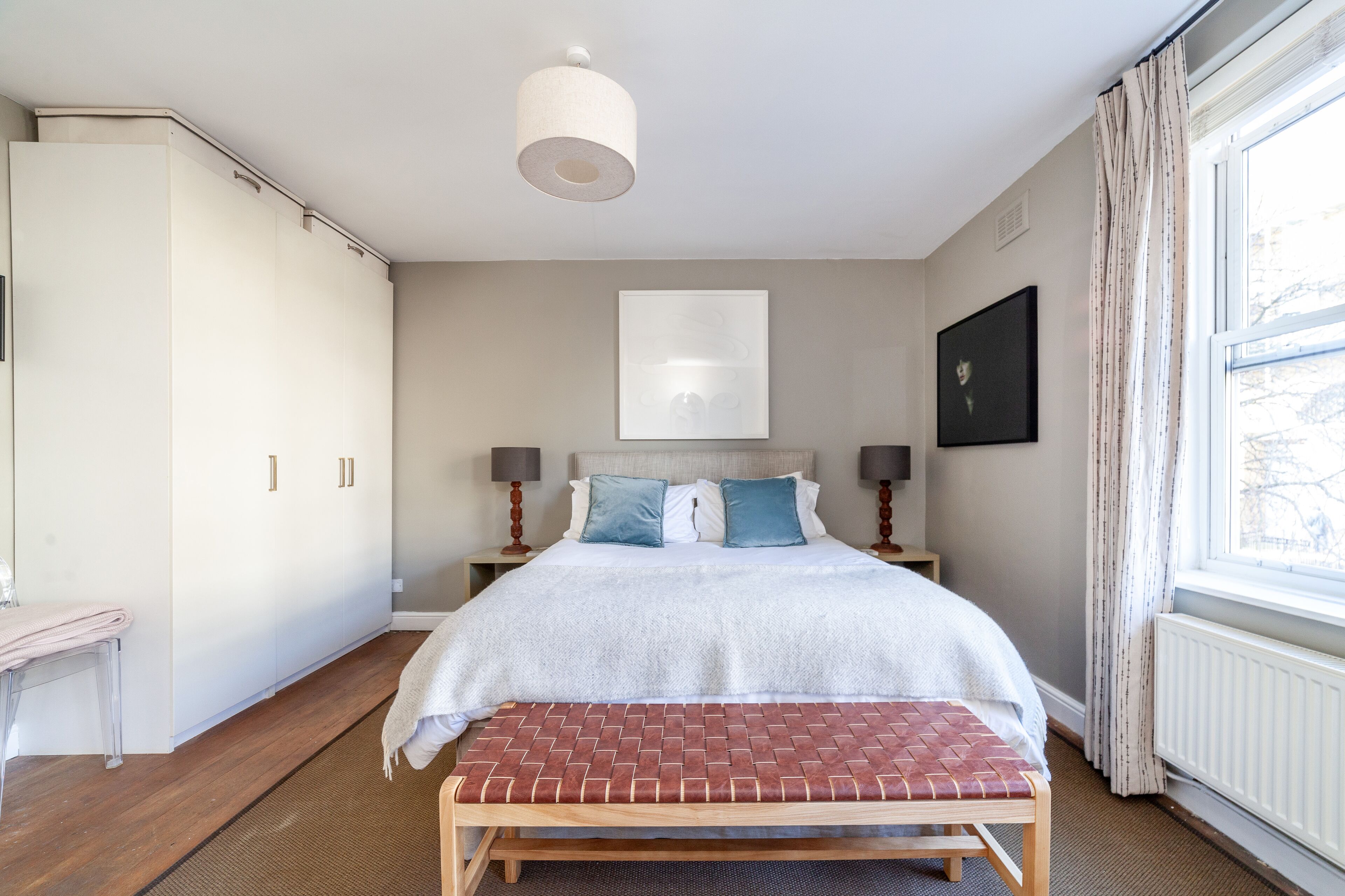 A bedroom with a bed, bench, wardrobe, bedside tables, and a window.