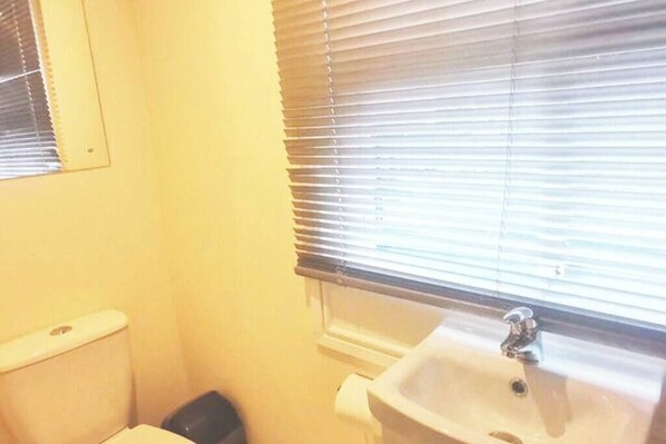 A small bathroom with a toilet, sink, and window with blinds.