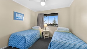 A room with two beds, a small table, a window with a view, and a ceiling fan. - Gena Apartments Unit 13 Kings Beach QLD (Kings Beach)