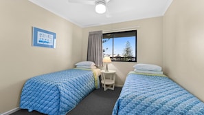 A room with two beds, a small table, a window with a view, and a ceiling fan.