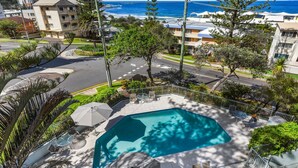 A residential area with a swimming pool, surrounded by trees and a view of the ocean. - Gena Apartments Unit 13 Kings Beach QLD (Kings Beach)