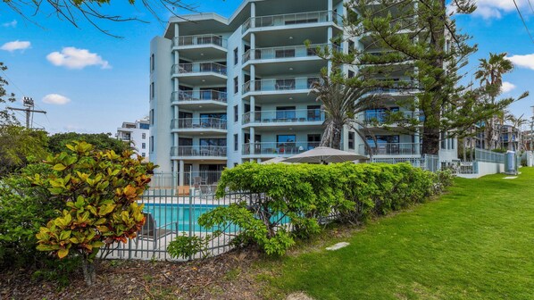 A multi-story hotel with balconies, a swimming pool, and lush greenery.