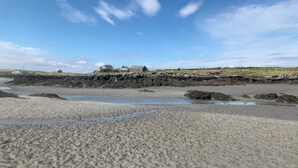 A beach with a rocky shoreline, a few buildings in the background, and a clear sky. - The Wheelhouse (Isle of North Uist)