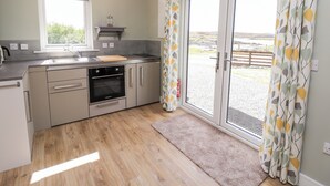 A modern kitchen with a built-in oven, a sink, and a window. - The Wheelhouse (Isle of North Uist)