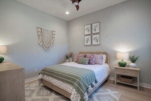 Ein Schlafzimmer mit einem Bett, Nachttischen, Wandbildern und einem Deckenventilator.