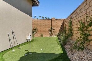 A backyard with artificial grass, a brick wall, and a small garden area with plants.