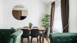 Ein Essbereich mit einem Holztisch, schwarzen Stühlen und grünen Polstersofas.