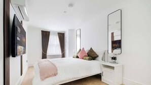 Ein modernes Schlafzimmer mit Bett, Nachttisch, Spiegel und einem an der Wand befestigten Fernseher.