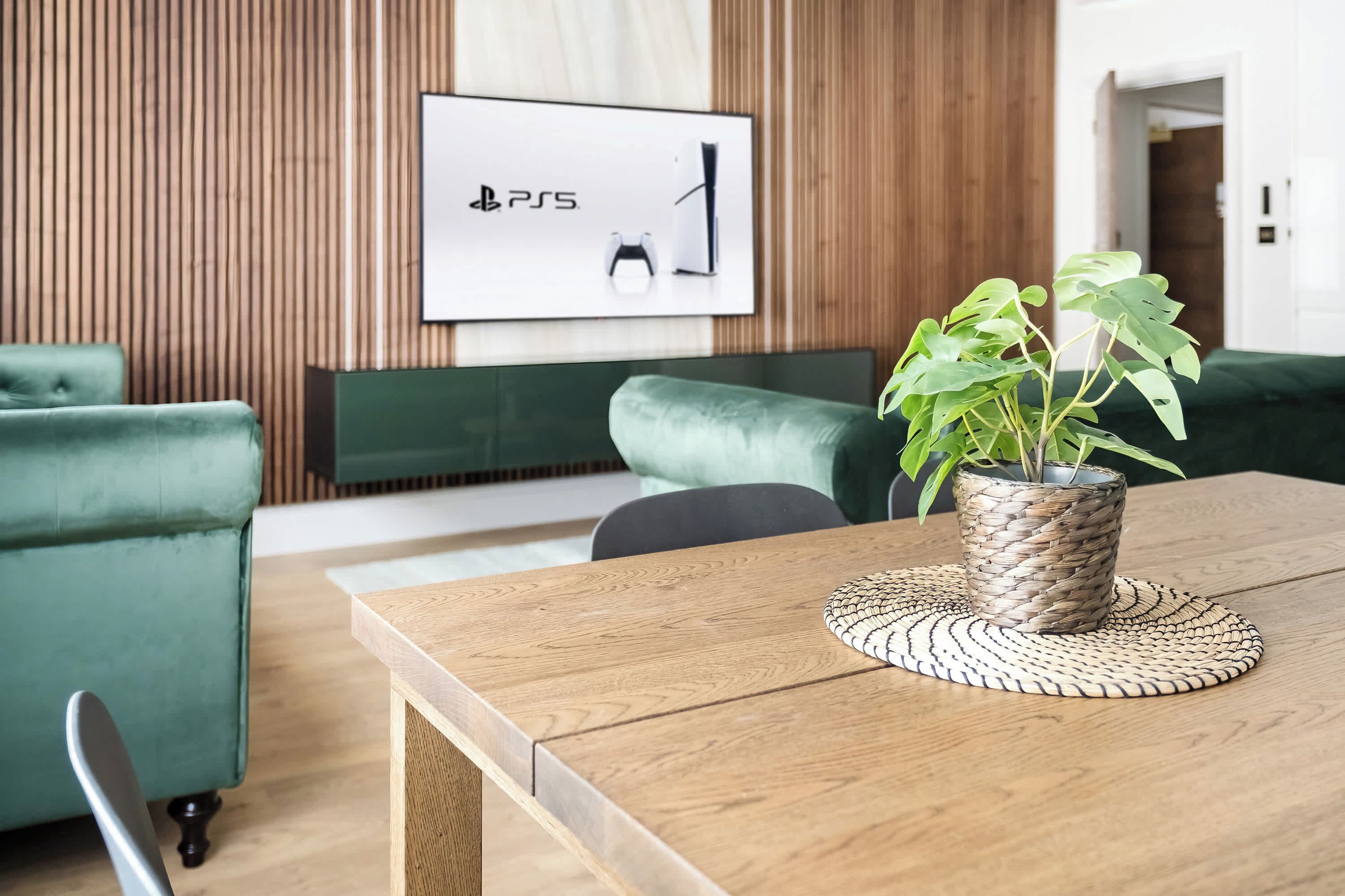 A modern living room with a wooden table, a green sofa, a green armchair, and a framed picture on the wall.