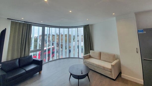 A modern living room with a curved glass wall, a black sofa, a beige sofa, and a round coffee table.