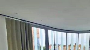 A room with a curved ceiling, large windows with curtains, and a view of buildings outside.
