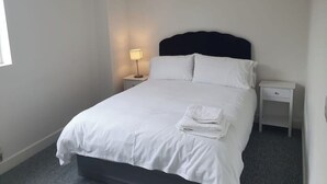 A neatly made bed with white linens, a dark headboard, and a small bedside table with a lamp.