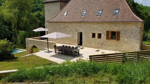A stone building with a tiled roof, a swimming pool, outdoor seating, and a wooden fence. - Moulin Proche Rivière Dans la Campagne Lotoise (Saint-Denis-Catus)