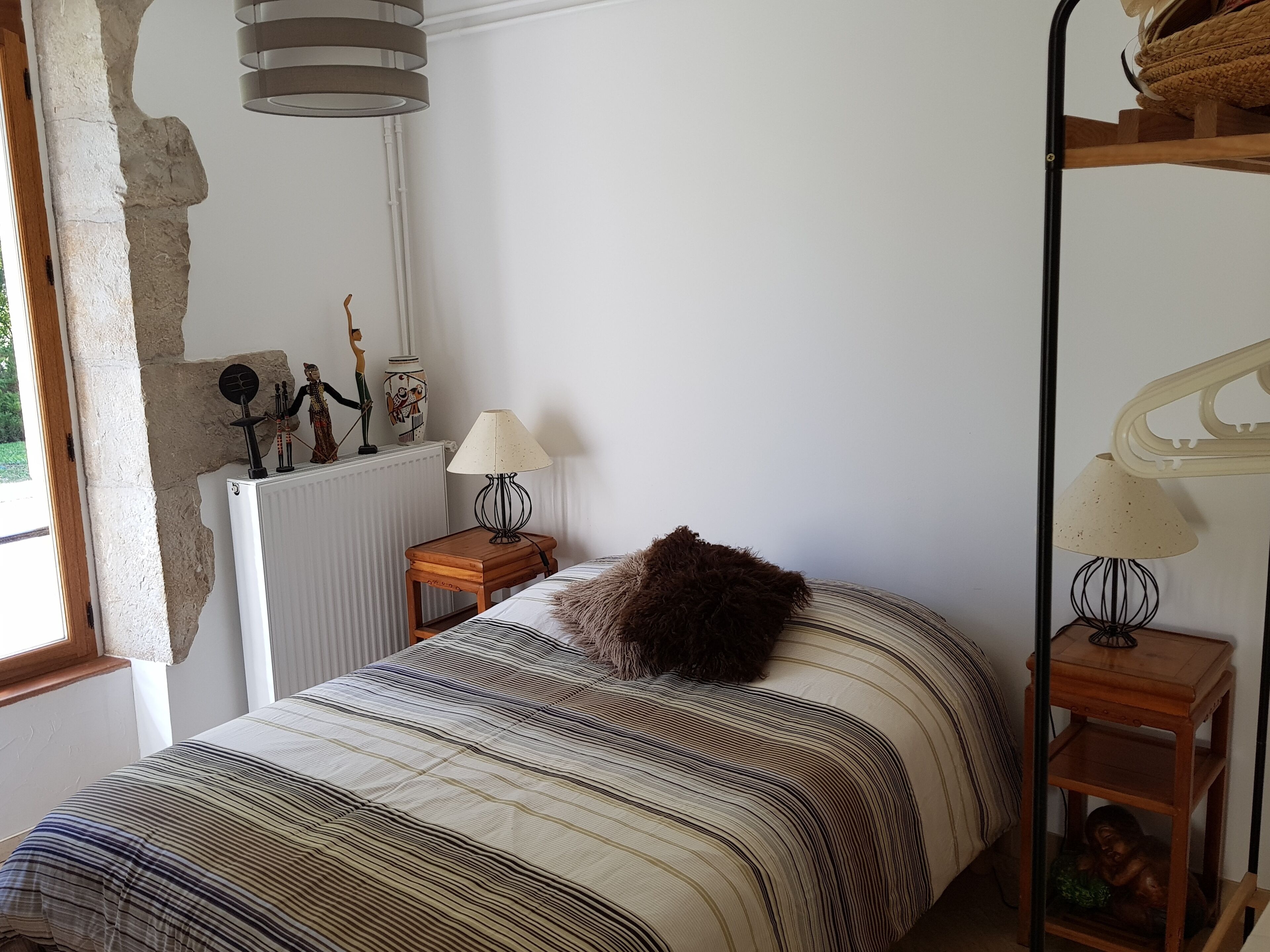 A bedroom with a bed, a lamp, a radiator, and a window.
