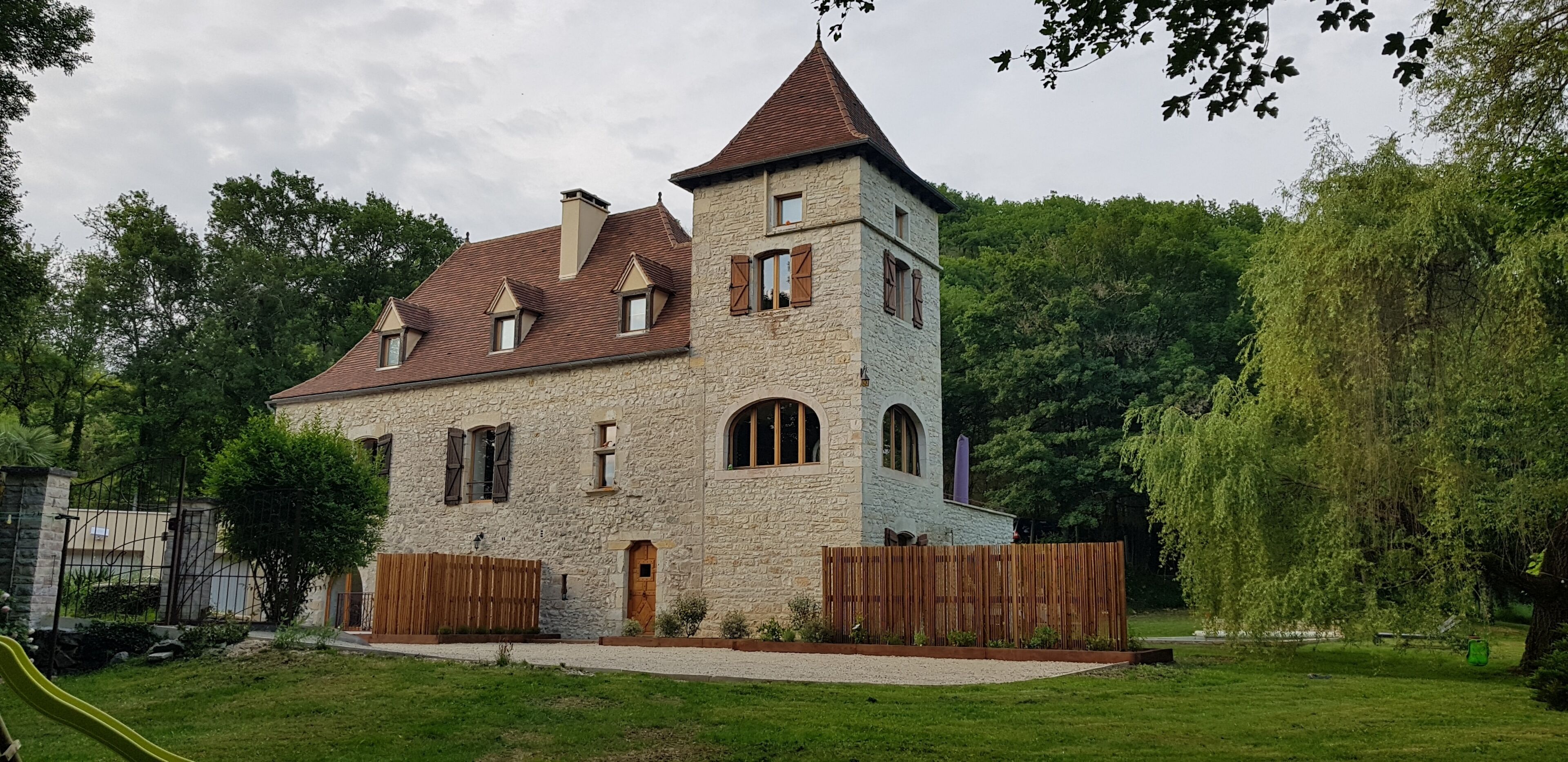 A stone building with a tower, a wooden fence, and a green lawn.