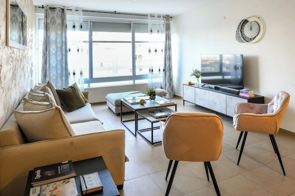 A living room with a sofa, two armchairs, a coffee table, a TV, and a window with curtains.