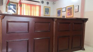 A wooden reception desk with framed pictures on the wall behind it. - Super OYO 152 Manam 1 Hotel Apartment (Muscat)