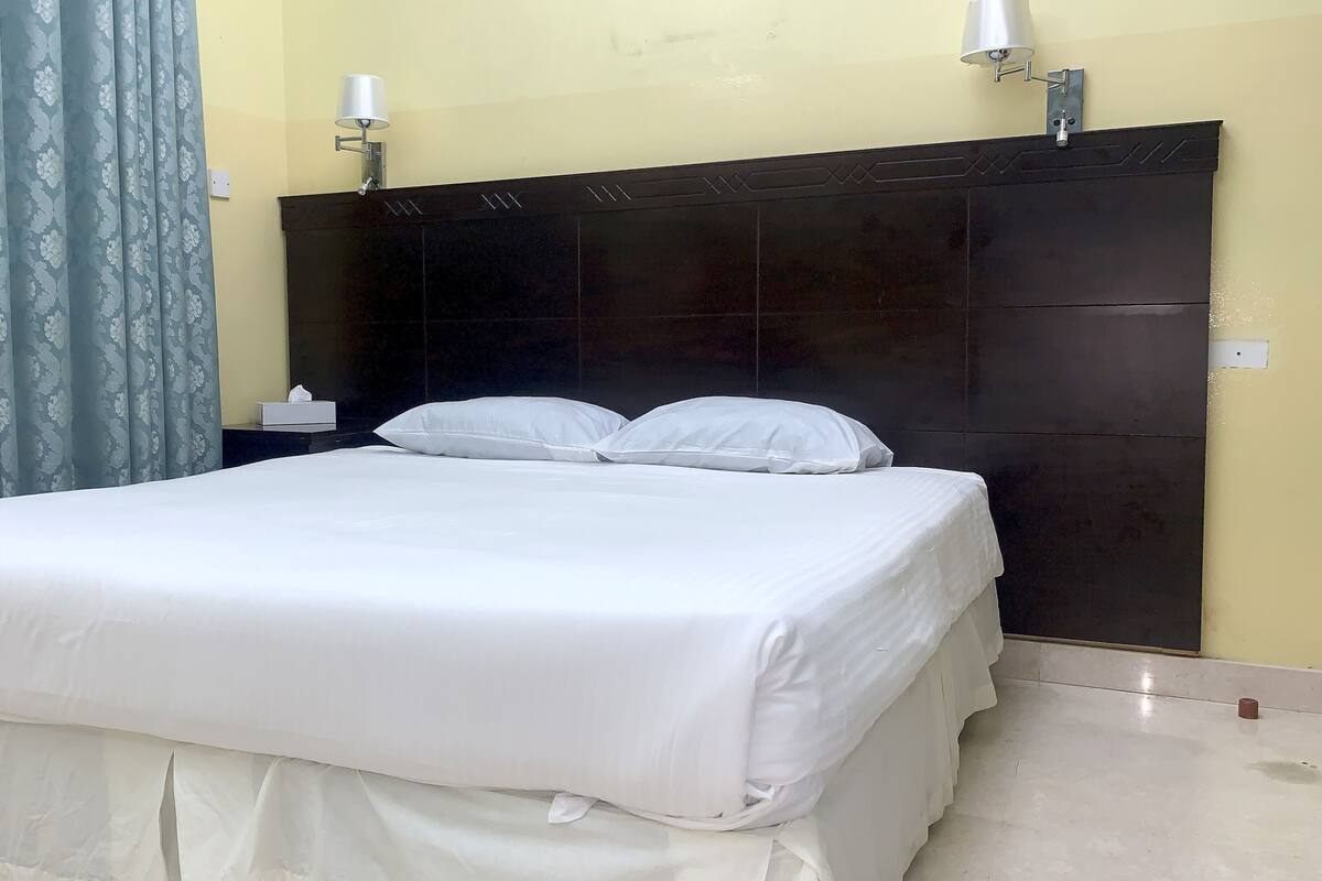 A neatly made bed with white linens, a dark headboard, and a small bedside table with a lamp.