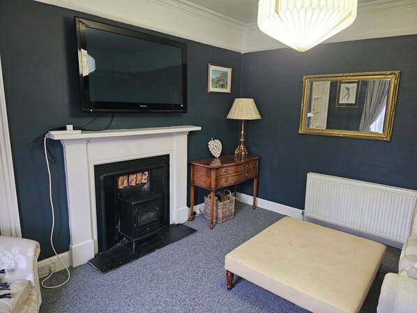 A room with a fireplace, a television mounted above it, a lamp, a bed, and a framed mirror on the wall.