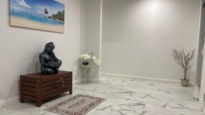 Un couloir doté d’un sol en marbre, d’un paillasson, d’une statue, d’un tableau et d’une plante en pot.