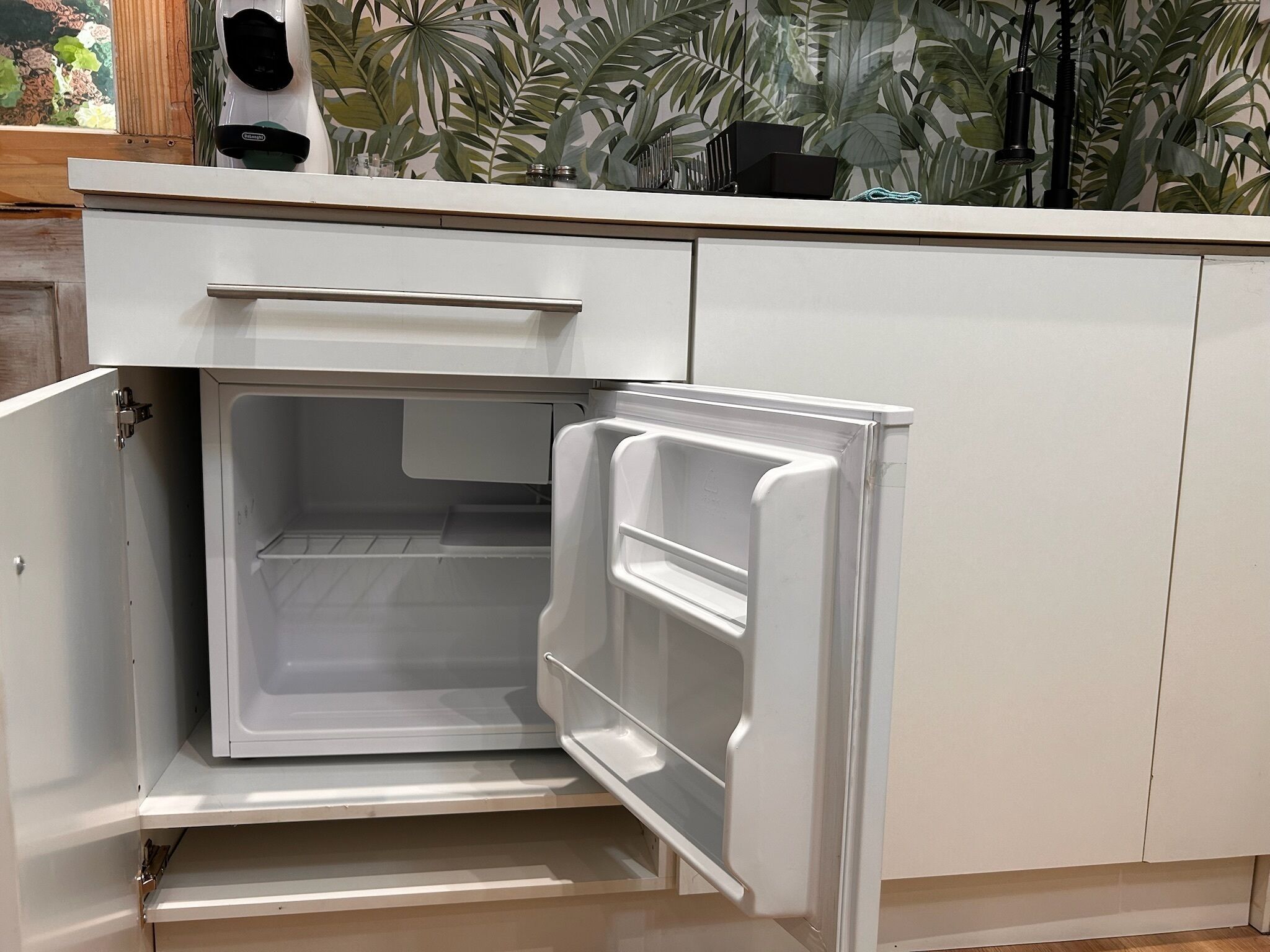 A white refrigerator with a freezer compartment, placed in a kitchen with white cabinets and a wooden countertop.