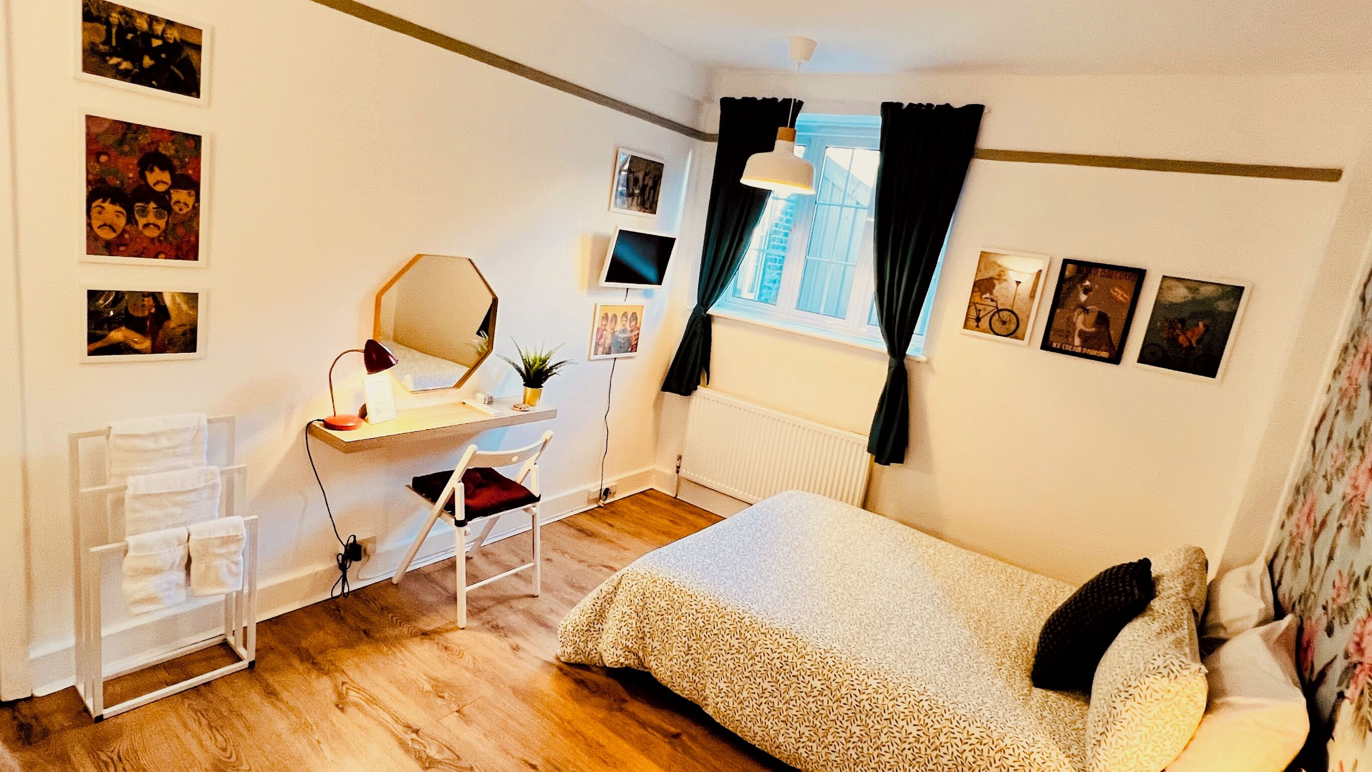 A bedroom with a bed, a desk with a chair, a mirror, and various pictures on the walls.