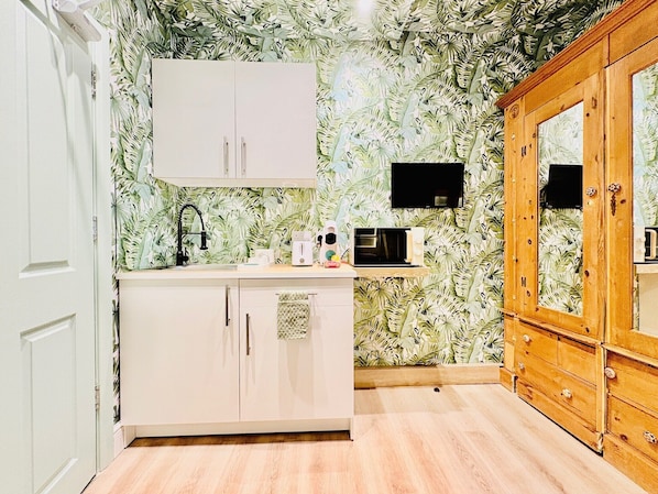 A compact kitchen with white cabinets, a microwave, and a wooden cabinet.