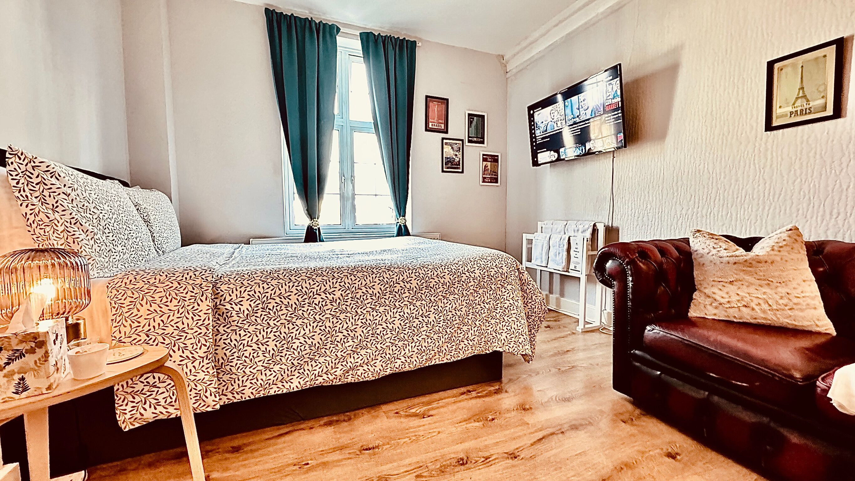 Un dormitorio con cama, sofá de cuero, televisión y ventana con cortinas.